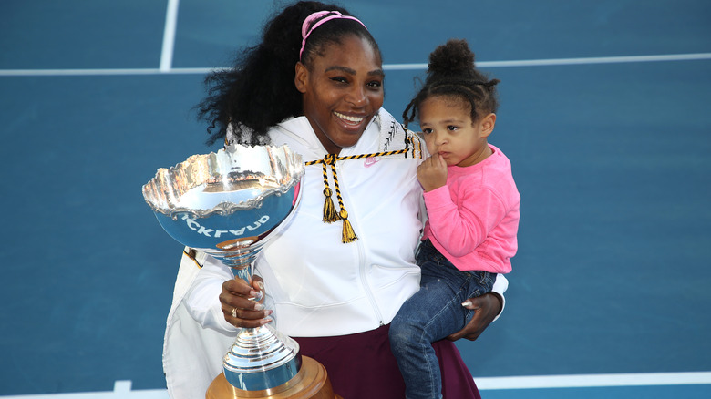 Serena Williams tiene in braccio sua figlia e un trofeo