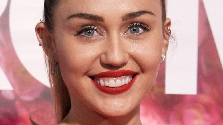 Miley Cyrus sorride sul red carpet con un rossetto rosso